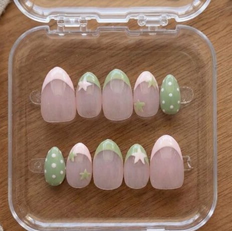 Ten almond press-on nails in sheer blush with sage green French tips, white stars, and polka-dot accents, in a clear case